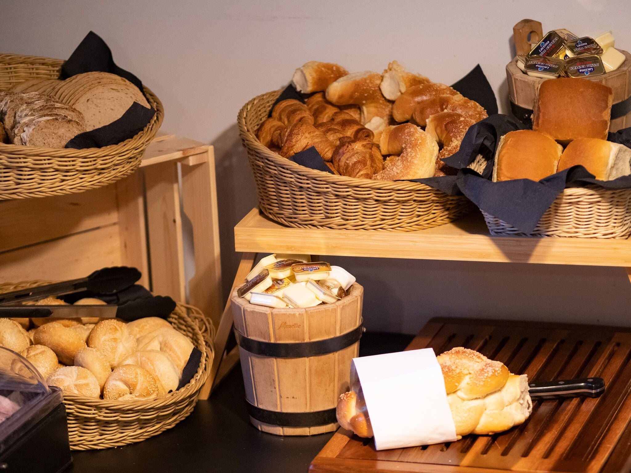 A buffet with various breads and pastries in baskets and wooden containers.