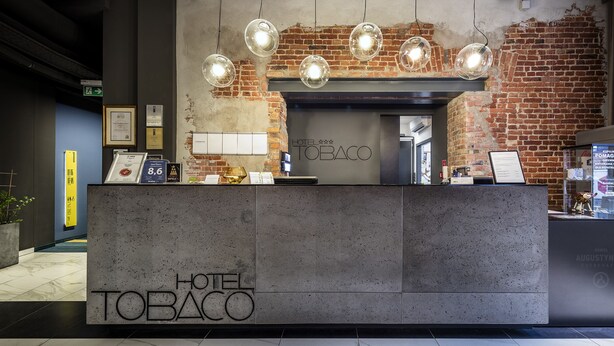 A reception desk at Hotel Tabo with a brick wall backdrop, a Coca-Cola refrigerator, and a framed certificate on the wall. - Hotel Tobaco (Lodz)
