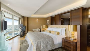 Habitación de hotel con una cama grande, un escritorio con silla, televisión y un ventanal con vistas a la ciudad.