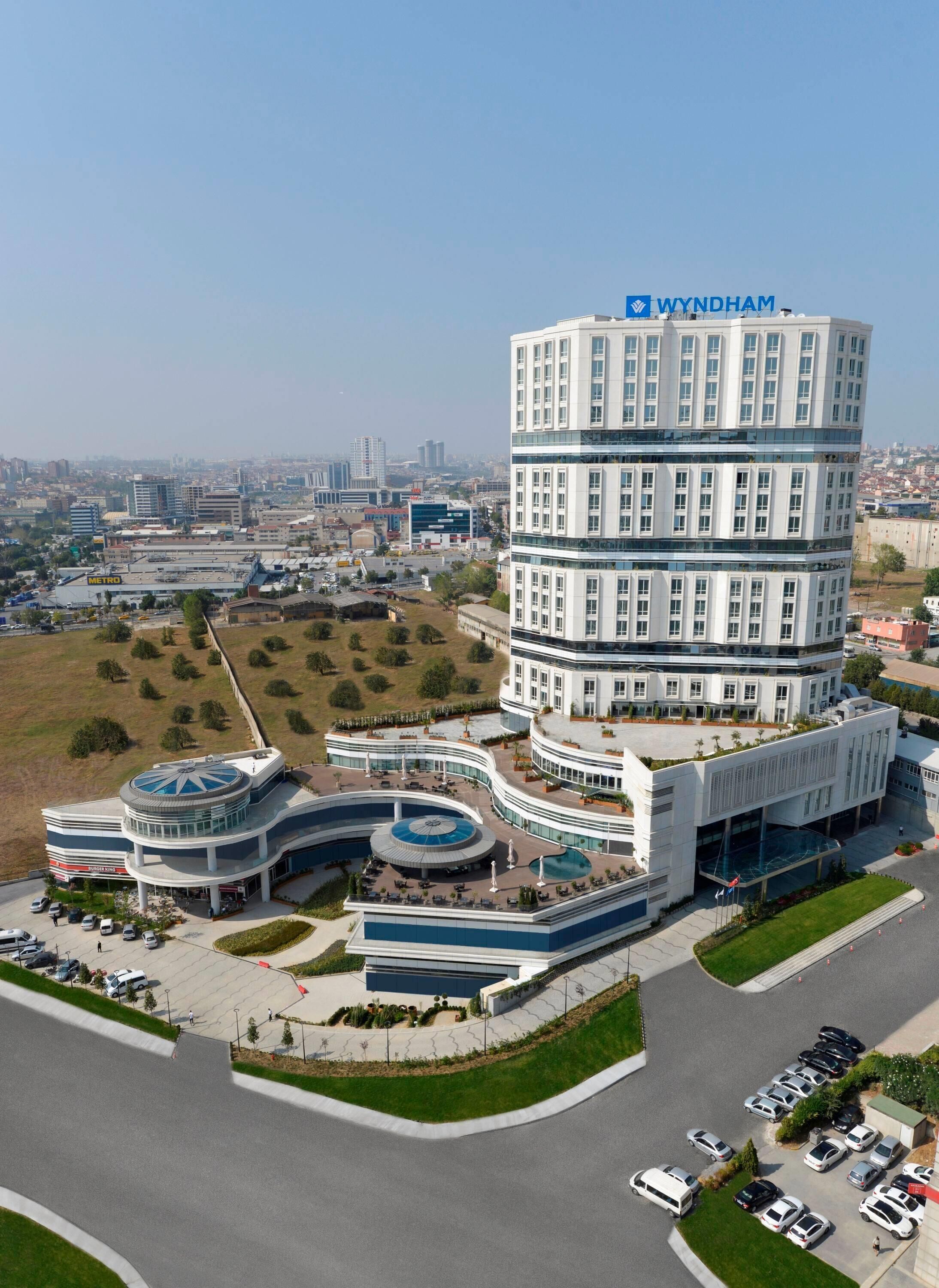 Un hotel de varios pisos con un llamativo letrero de 'Wyndham', que cuenta con un patio central con piscina circular y zonas de estar alrededor.