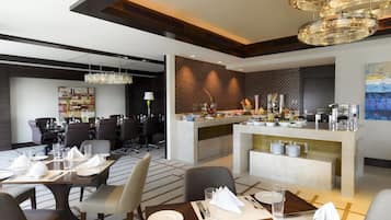 Un comedor de hotel moderno con una barra central, varias mesas dispuestas para comer y una lámpara contemporánea.
