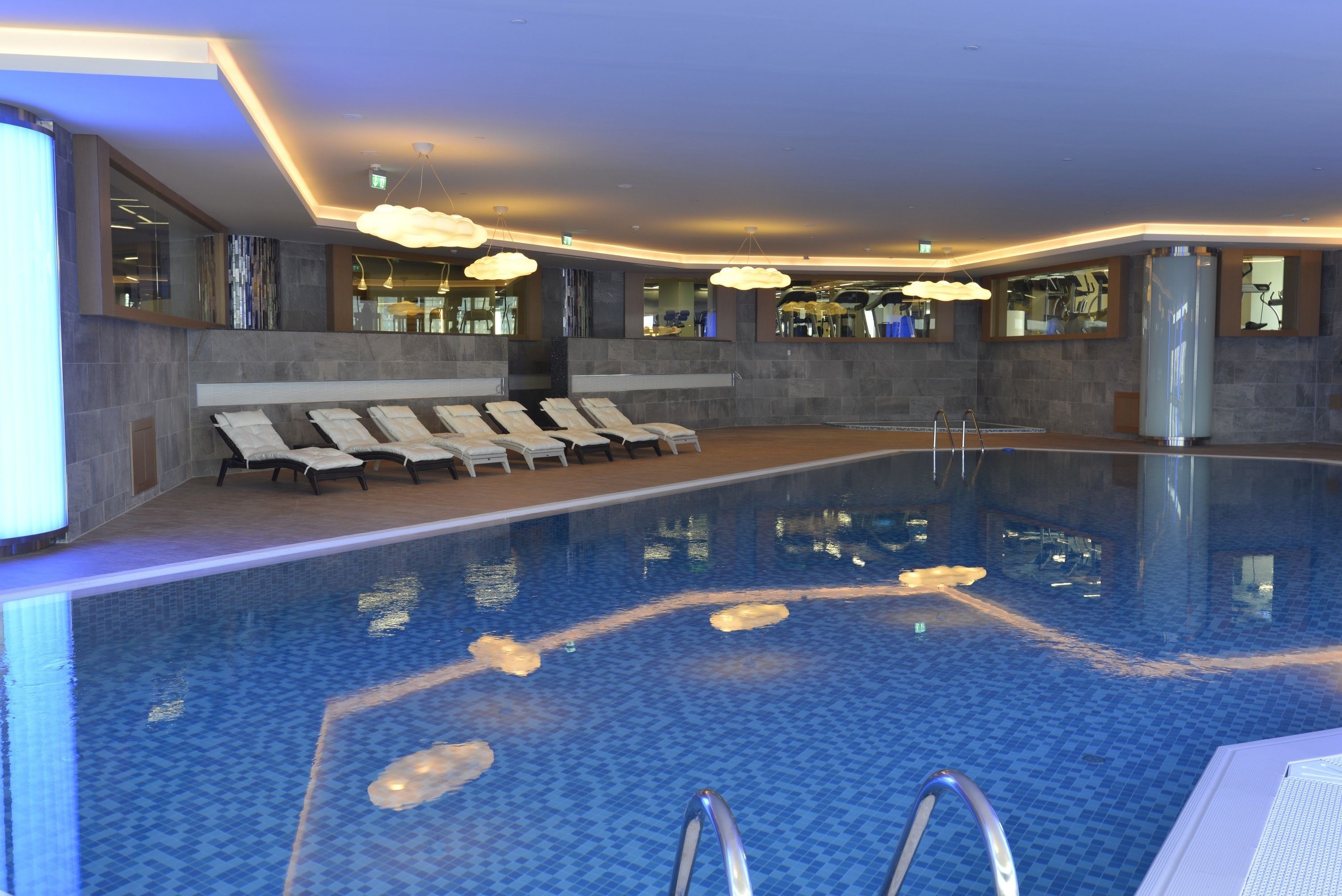 Una piscina interior moderna con sillones de descanso y zona acuática transparente.