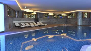Una piscina interior moderna con sillones de descanso y zona acuática transparente.
