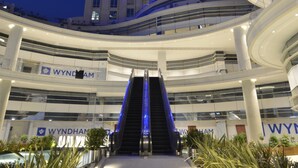 Un atrio de varios niveles con una escalera central, rodeado de plantas y con señalización de hoteles Wyndham.