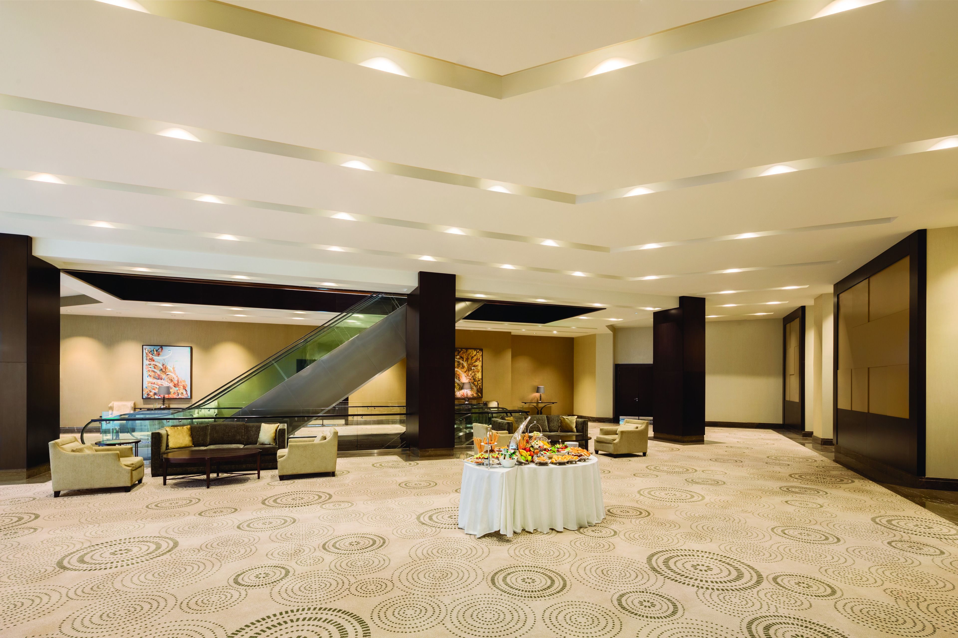 A spacious lobby with a central seating area, a buffet table, and an escalator.