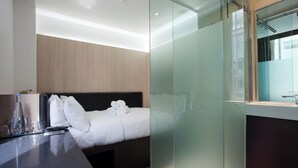 A modern hotel room with a bed, bedside table, and a glass partition. - The Z Hotel Victoria (London)