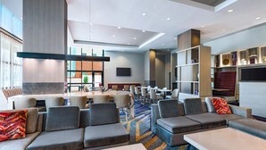 Eine moderne Hotelhalle mit Barbereich, Sitzgelegenheiten und einem Fernsehbildschirm.