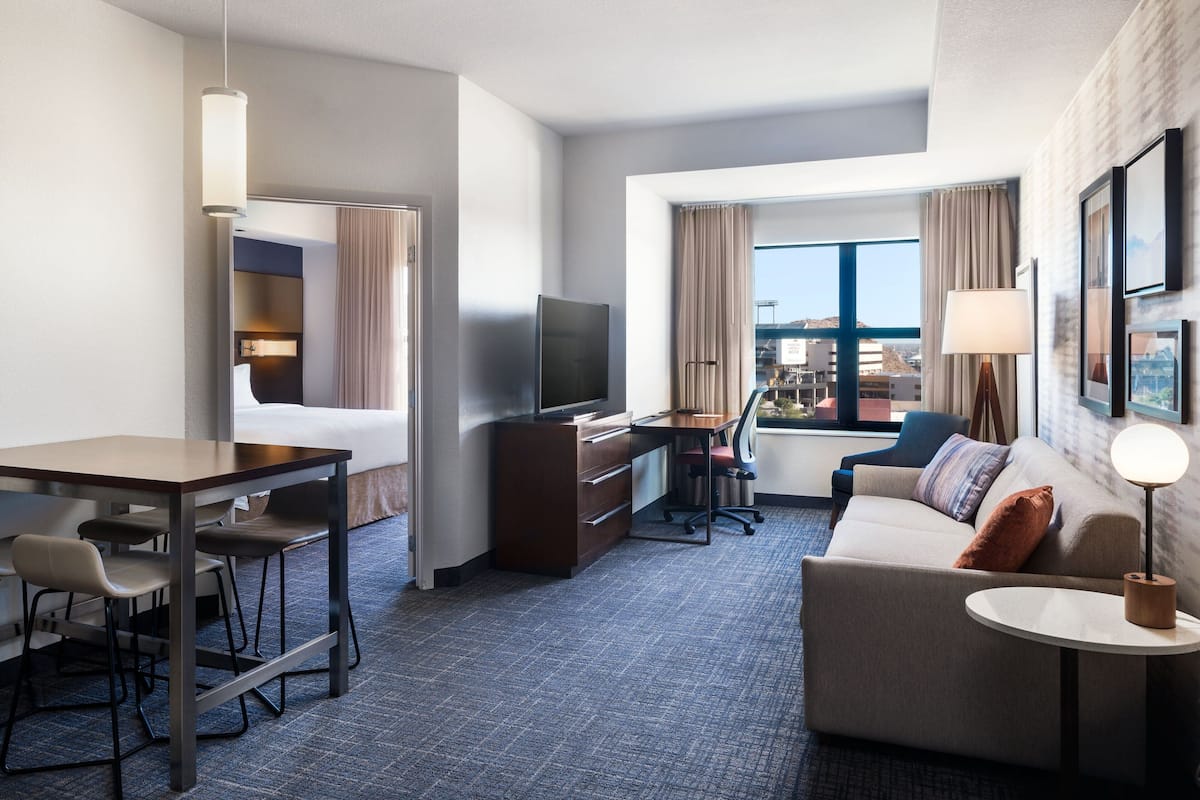 Une chambre d’hôtel avec un lit, un bureau avec un ordinateur, une télévision, un canapé et une fenêtre avec des rideaux.