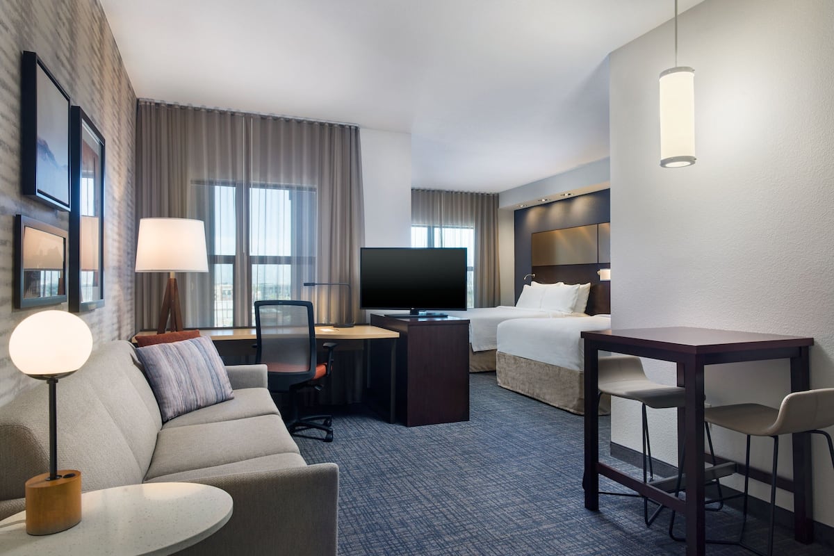 Une chambre d’hôtel comprenant un canapé, un bureau avec une chaise, une télévision, un lit et une petite table avec des chaises.