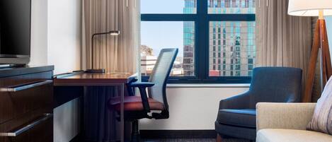 A hotel room with a desk, office chair, sofa, and a television.