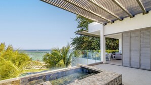 Un área de piscina moderna al aire libre con vistas despejadas al océano, un espacio de descanso cubierto y un amplio ventanal corredera que da a un patio.