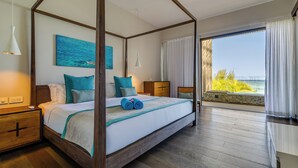 Una cama con dosel y vistas al océano, una mesita de noche de madera y un amplio ventanal con cortinas.