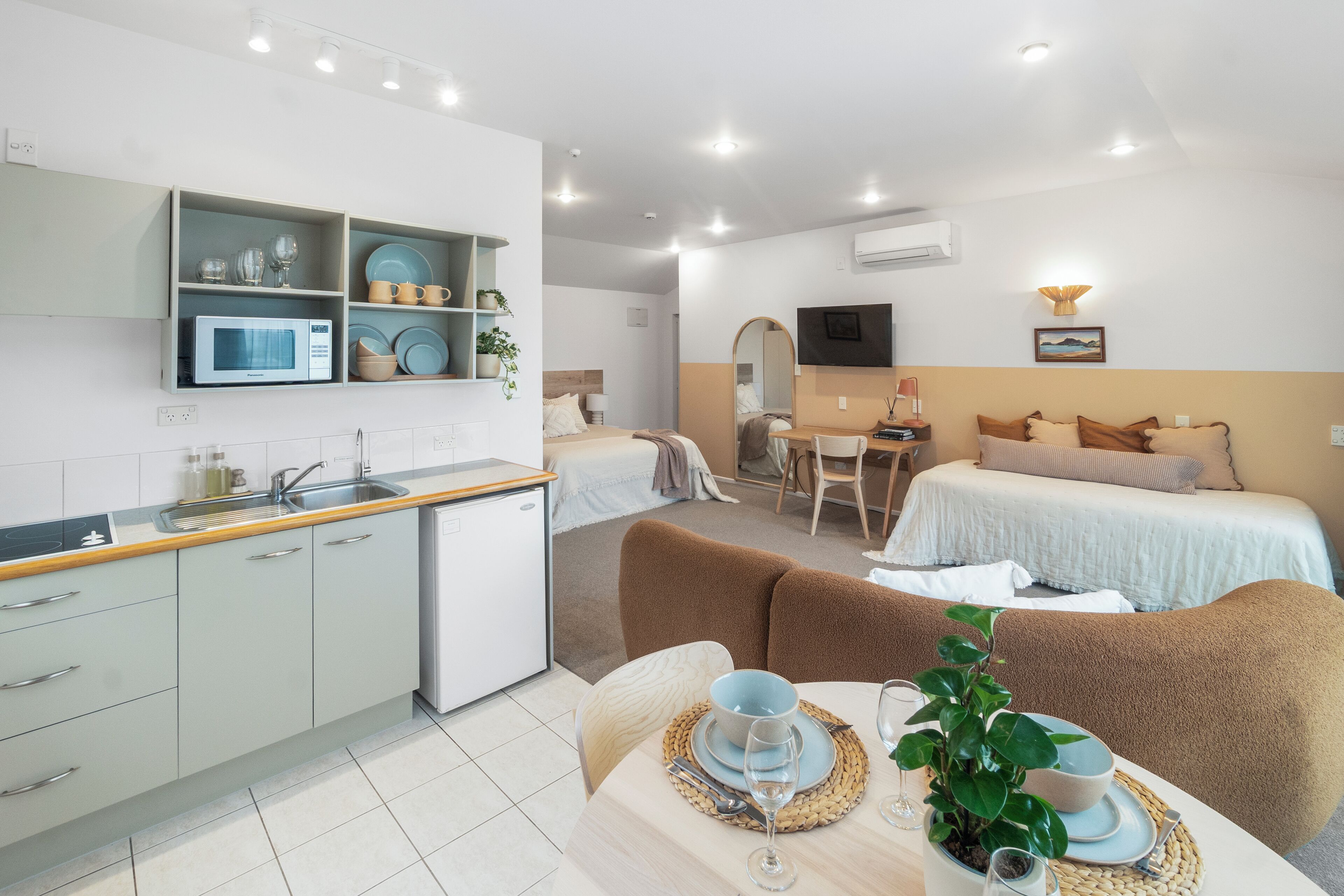 A modern hotel room with a kitchenette, a dining area, and a bed.