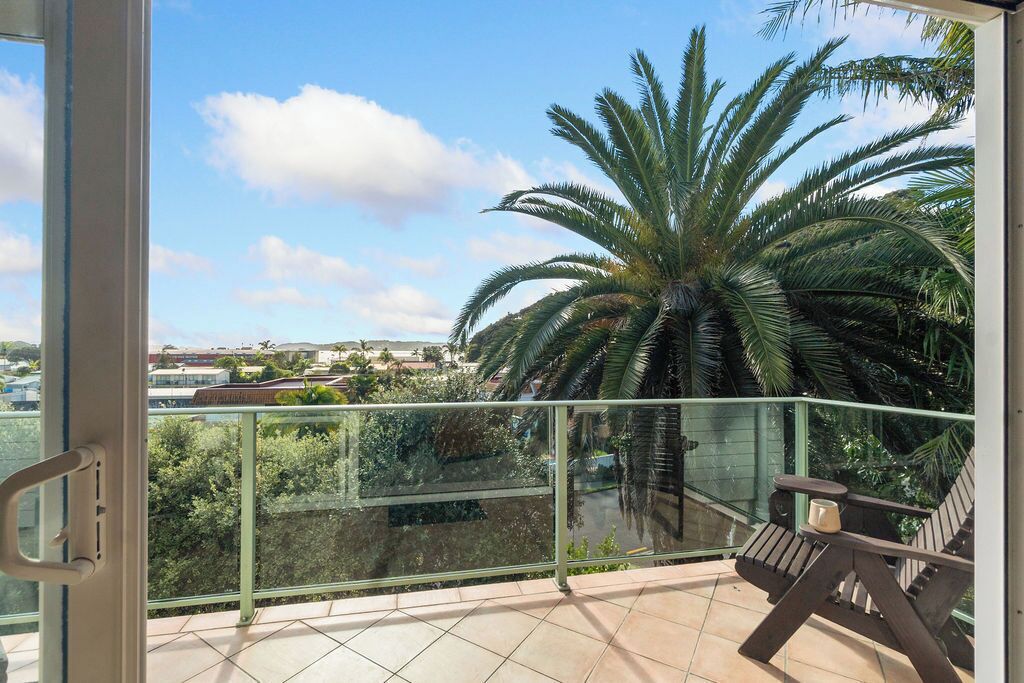A balcony with a glass railing, a wooden chair, and a large palm tree.