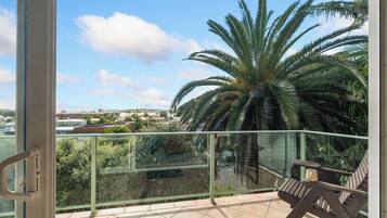 A balcony with a glass railing, a wooden chair, and a large palm tree.