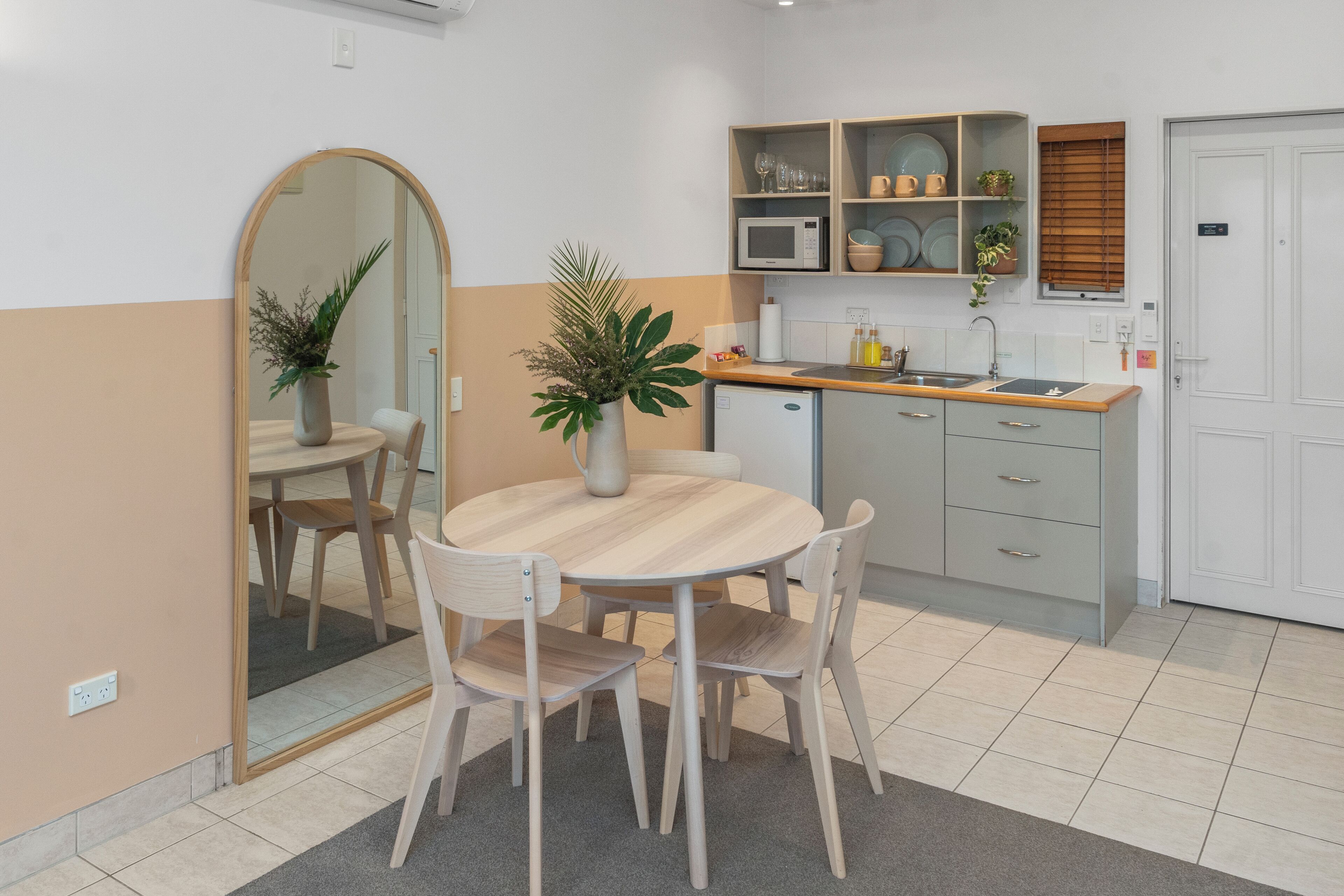 A modern kitchen with a round wooden table, four chairs, a microwave, a sink, and a cabinet with dishes.
