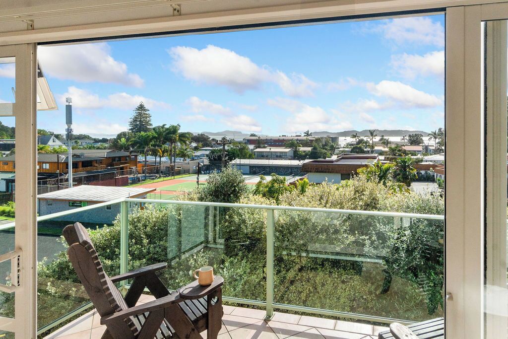 Un balcon donnant sur un terrain de sport, une chaise et une table avec une tasse.