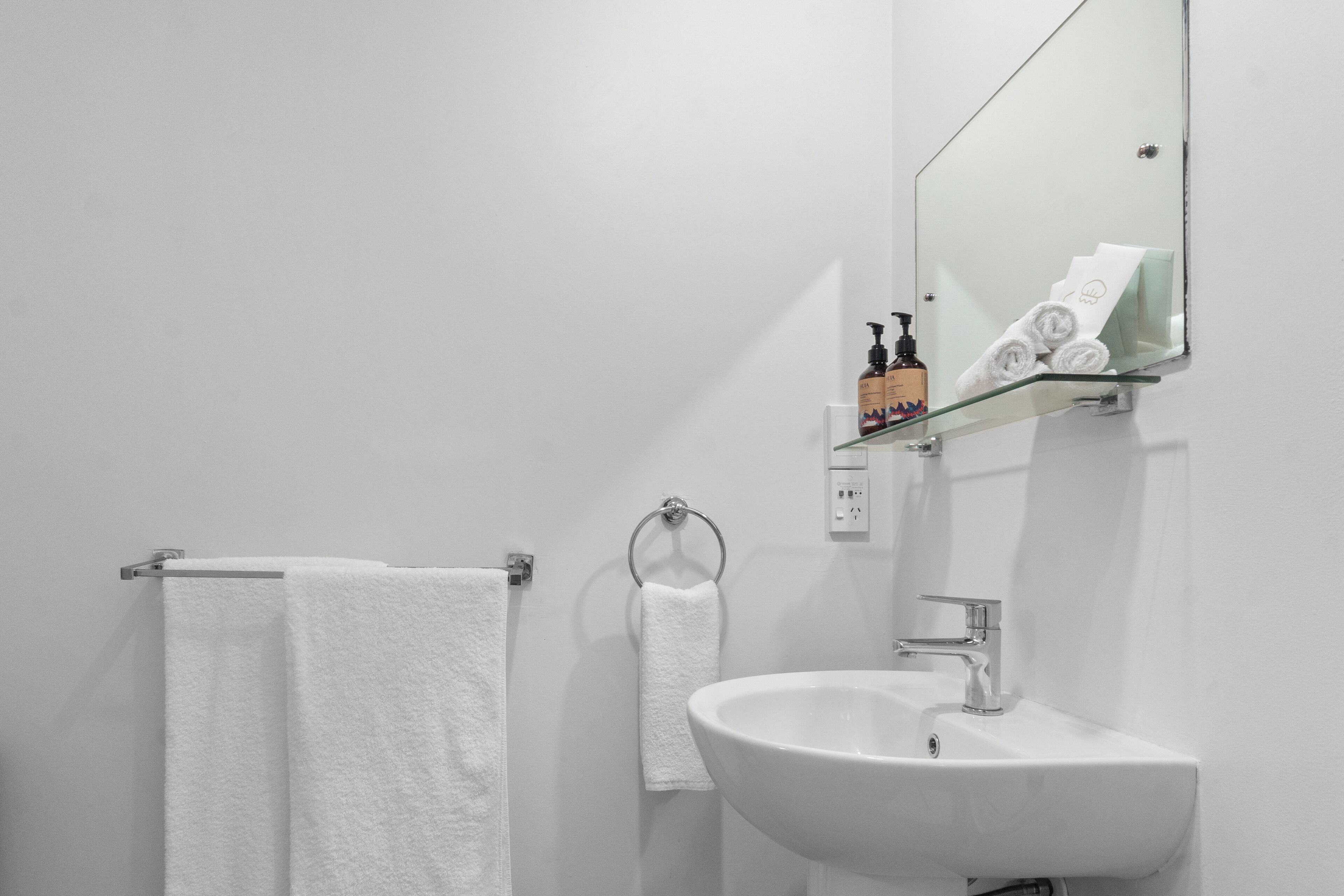 A modern bathroom with a white sink, a glass shelf, and two white towels hanging on a metal towel ring.