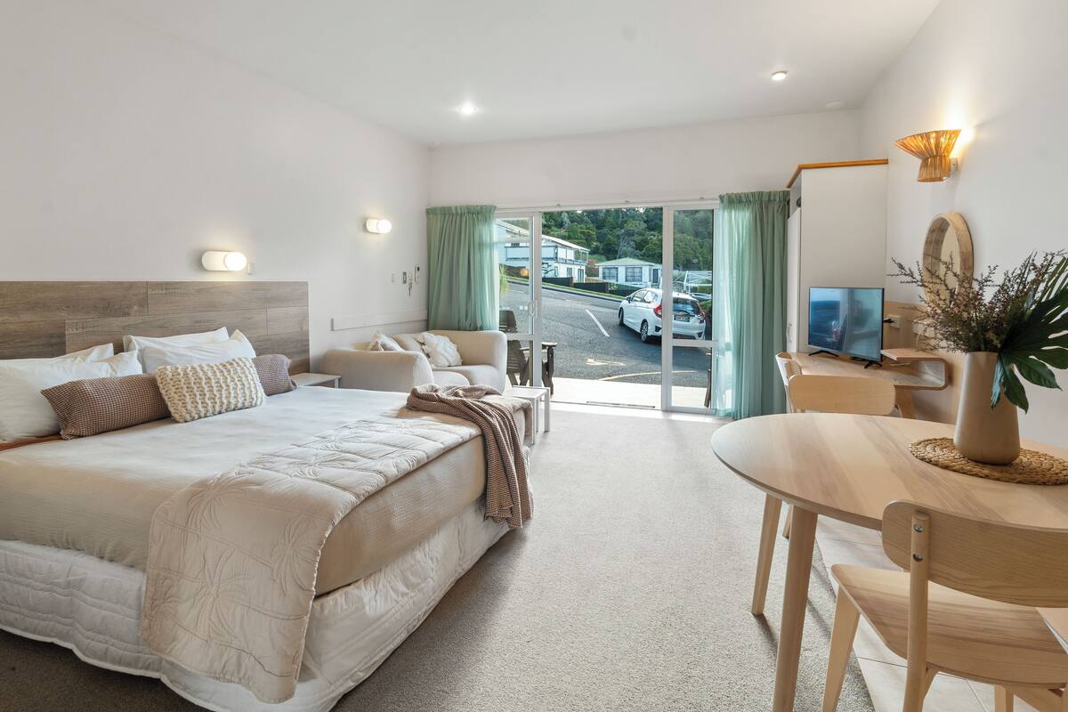 A hotel room with a bed, a desk, a chair, a TV, and a view of the street.