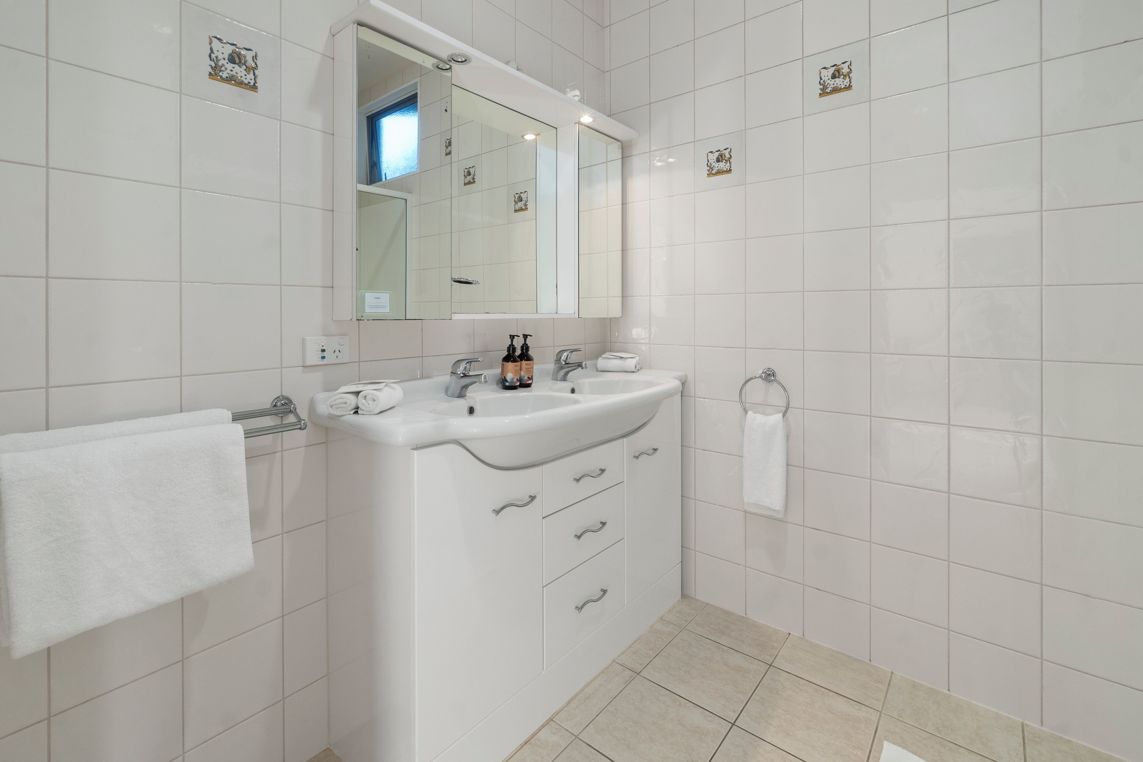 A modern bathroom with white tiles, a large mirror, a sink with a towel rack, and a toilet with a towel.