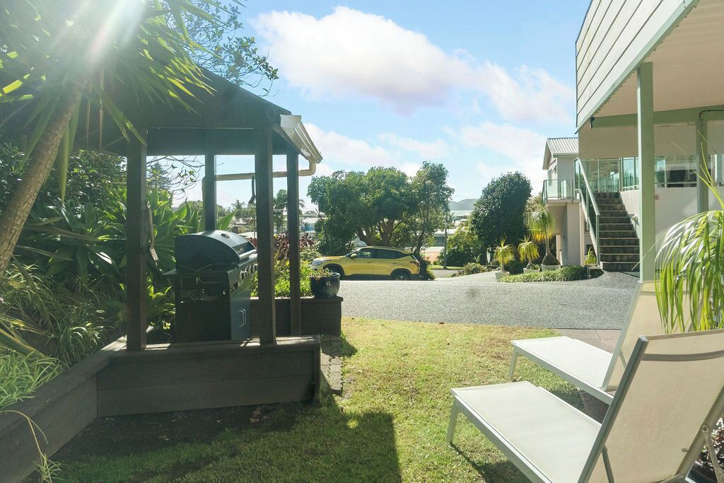 A covered outdoor area with a barbecue grill, a lawn chair, and a pathway leading to a building with a staircase.