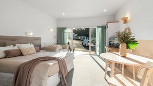 A bedroom with a large bed, a dining table, and a view of the street outside. - ASURE Admirals View Motel (Paihia)