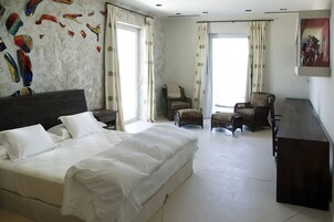 Ein Hotelzimmer mit einem großen Bett, zwei Sesseln, einem kleinen Tisch und einem Schreibtisch.
