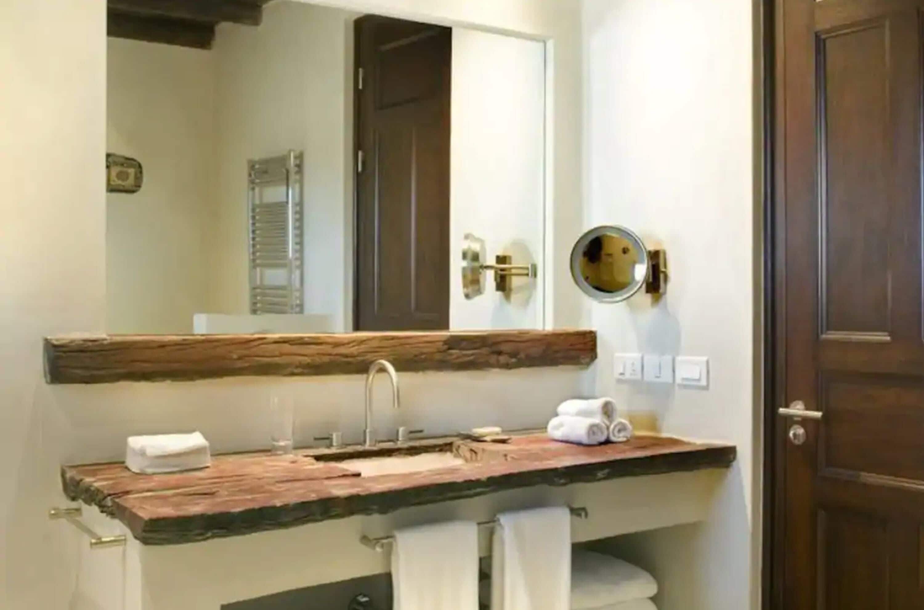 Un baño con tocador de madera, espejo, toallero y puerta.