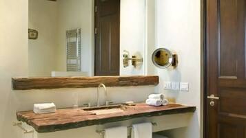 Un baño con tocador de madera, espejo, toallero y puerta.