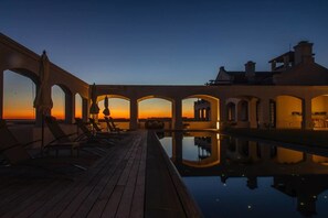 A serene pool area with a wooden deck and lounge chairs, surrounded by arched structures and a sunset view. - Estancia Vik Jose Ignacio (José Ignacio)