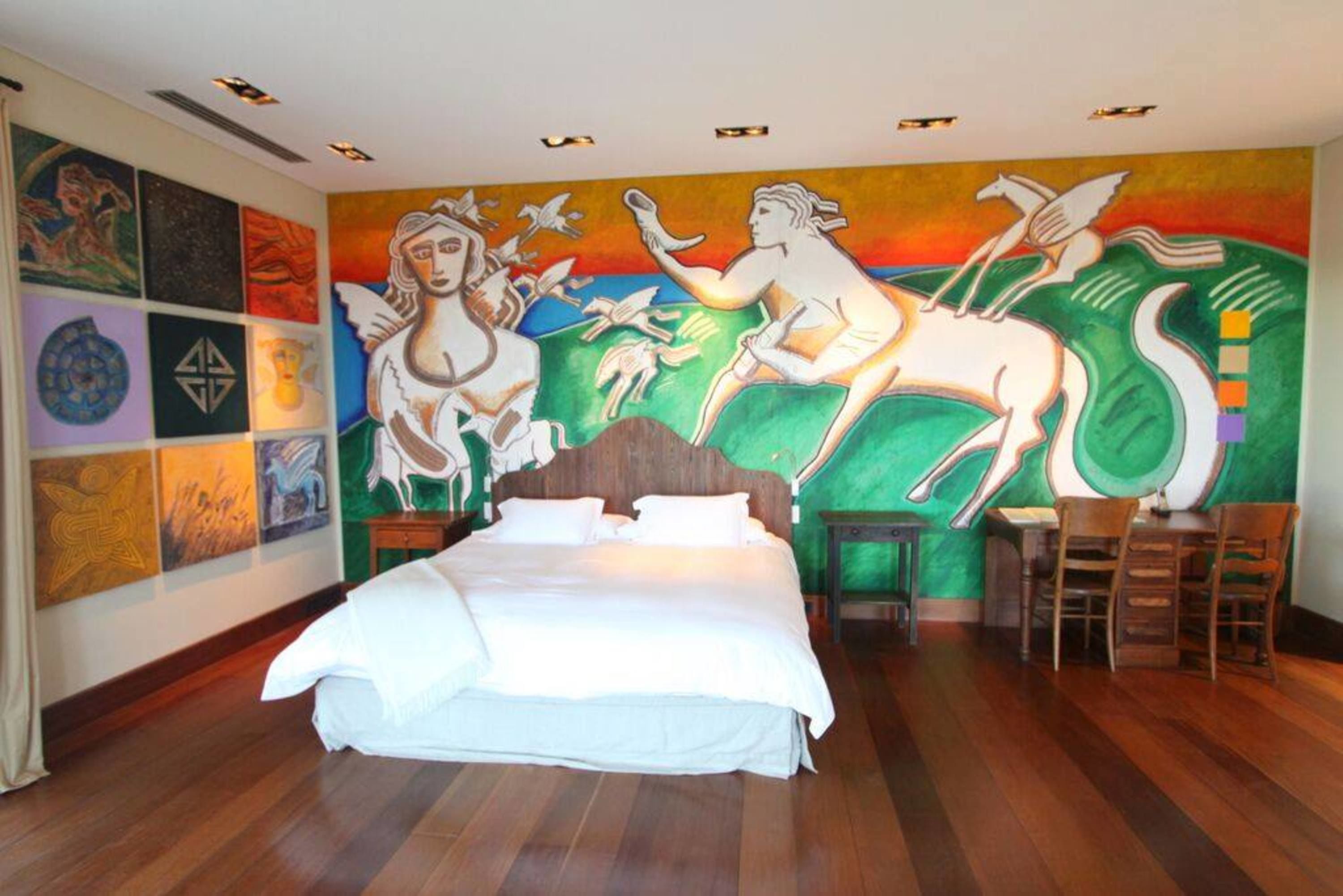 A bedroom with a large bed, a mural on the wall, and a small table with chairs.