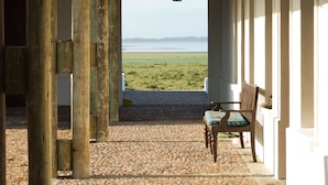 Un espacio al aire libre techado con vista al mar, columnas de madera, un farol y un banco.