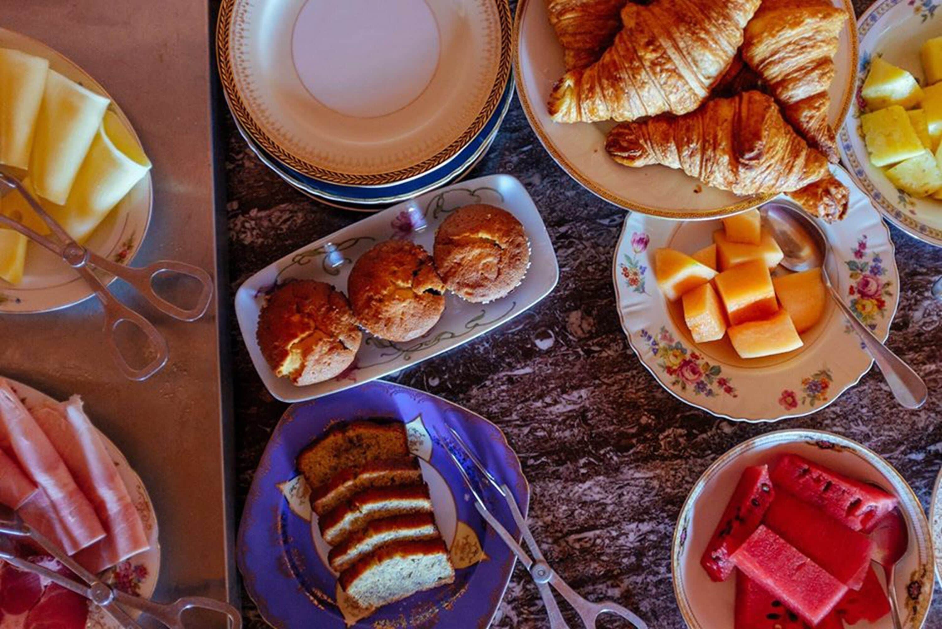 Uma mesa com diversos alimentos, incluindo croissants, fruta e bolo.