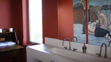 A bathroom with a large mirror, a sink with three faucets, and a painting of a nude couple on the wall.