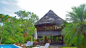 A two-story building with a thatched roof, surrounded by lush greenery and a swimming pool with lounge chairs. - Suchipakari Jungle Lodge (Misahualli)