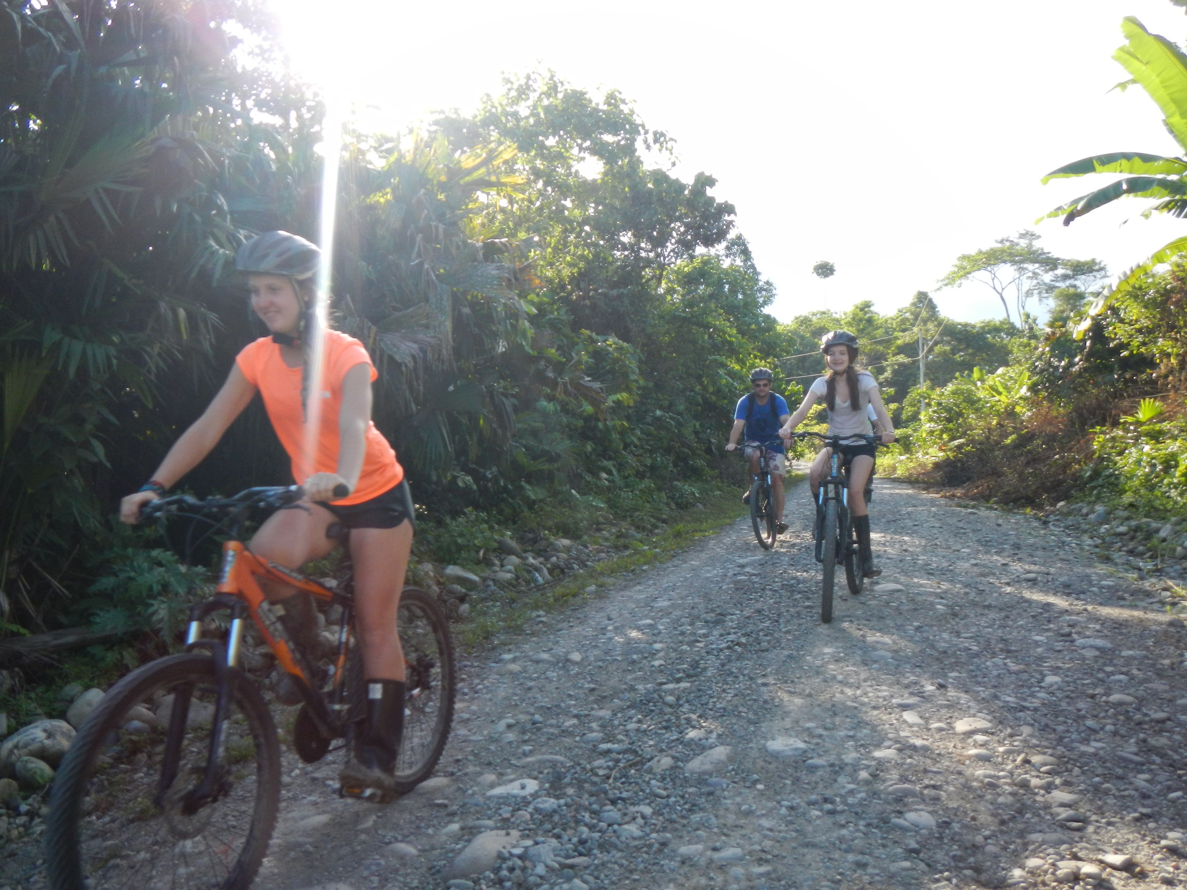 Trois personnes font du vélo sur un chemin de gravier, entourées de verdure.