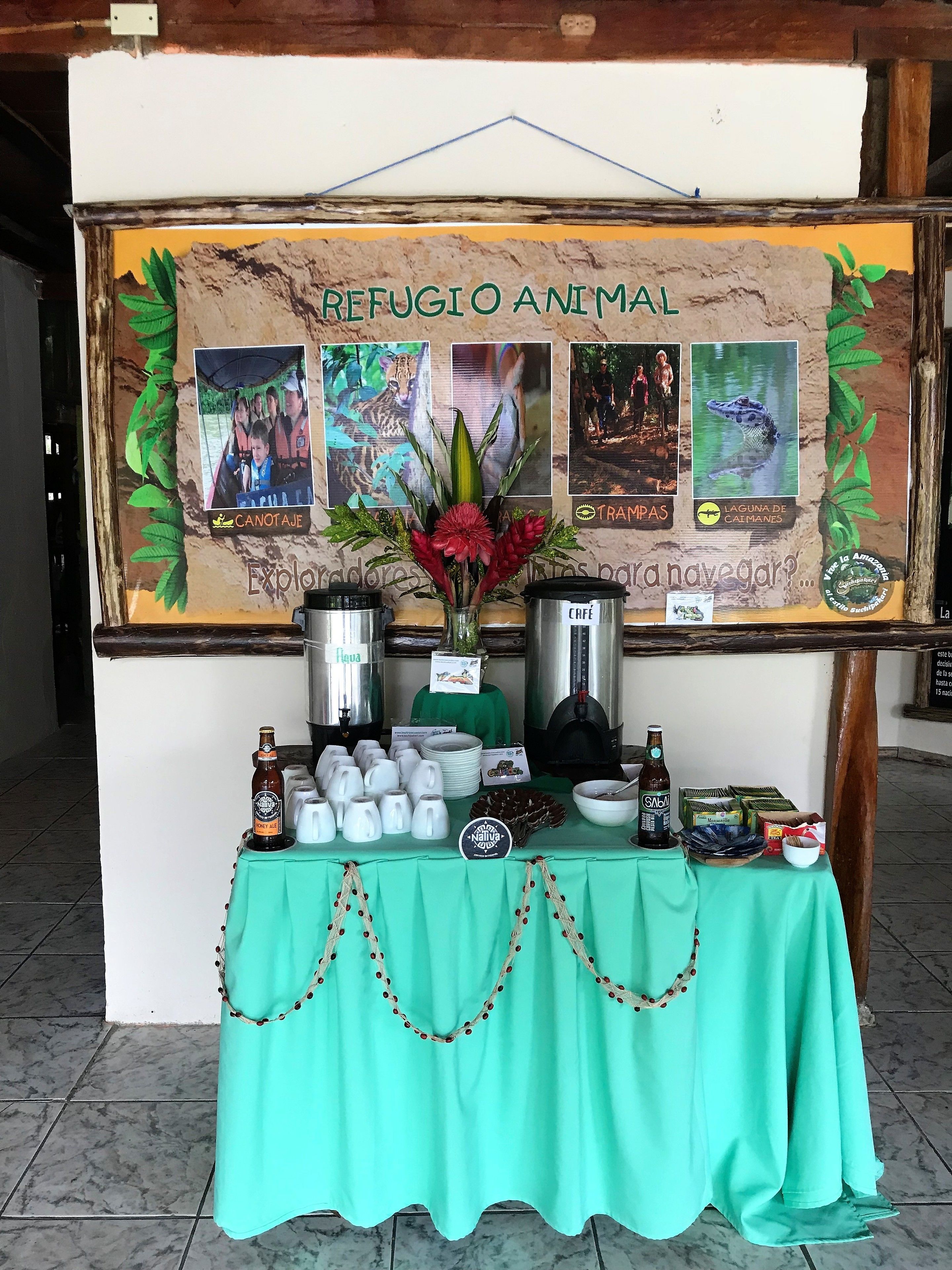 A booth with a sign reading "REFUGIO ANIMAL" featuring animal photos and a flower arrangement. It has a table with coffee pots, mugs, and snacks.