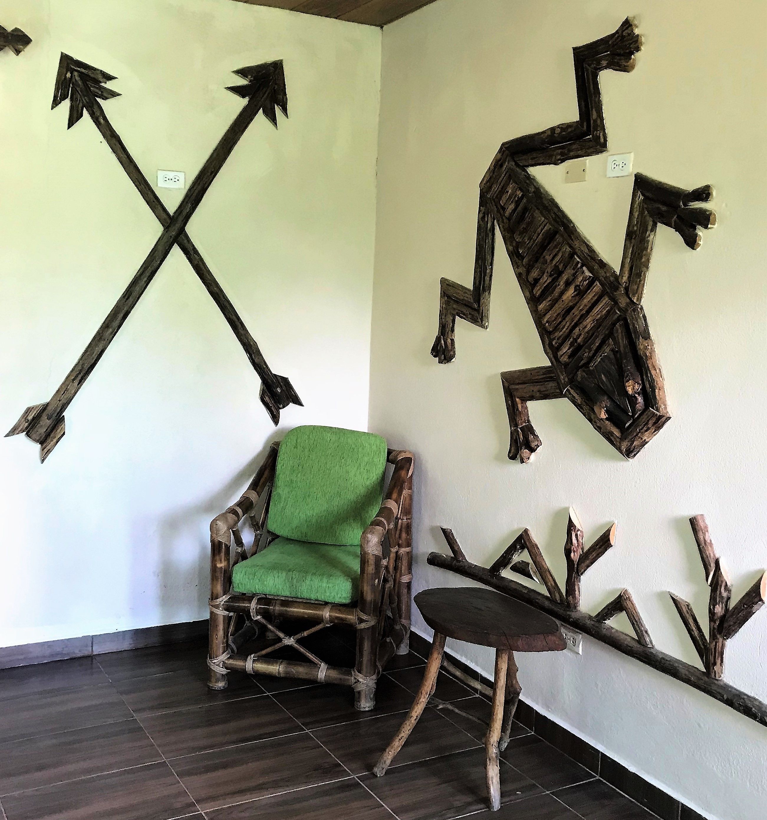 Una habitación con una silla de madera con cojín verde, un taburete pequeño y una obra de arte en la pared con flechas y formas abstractas.