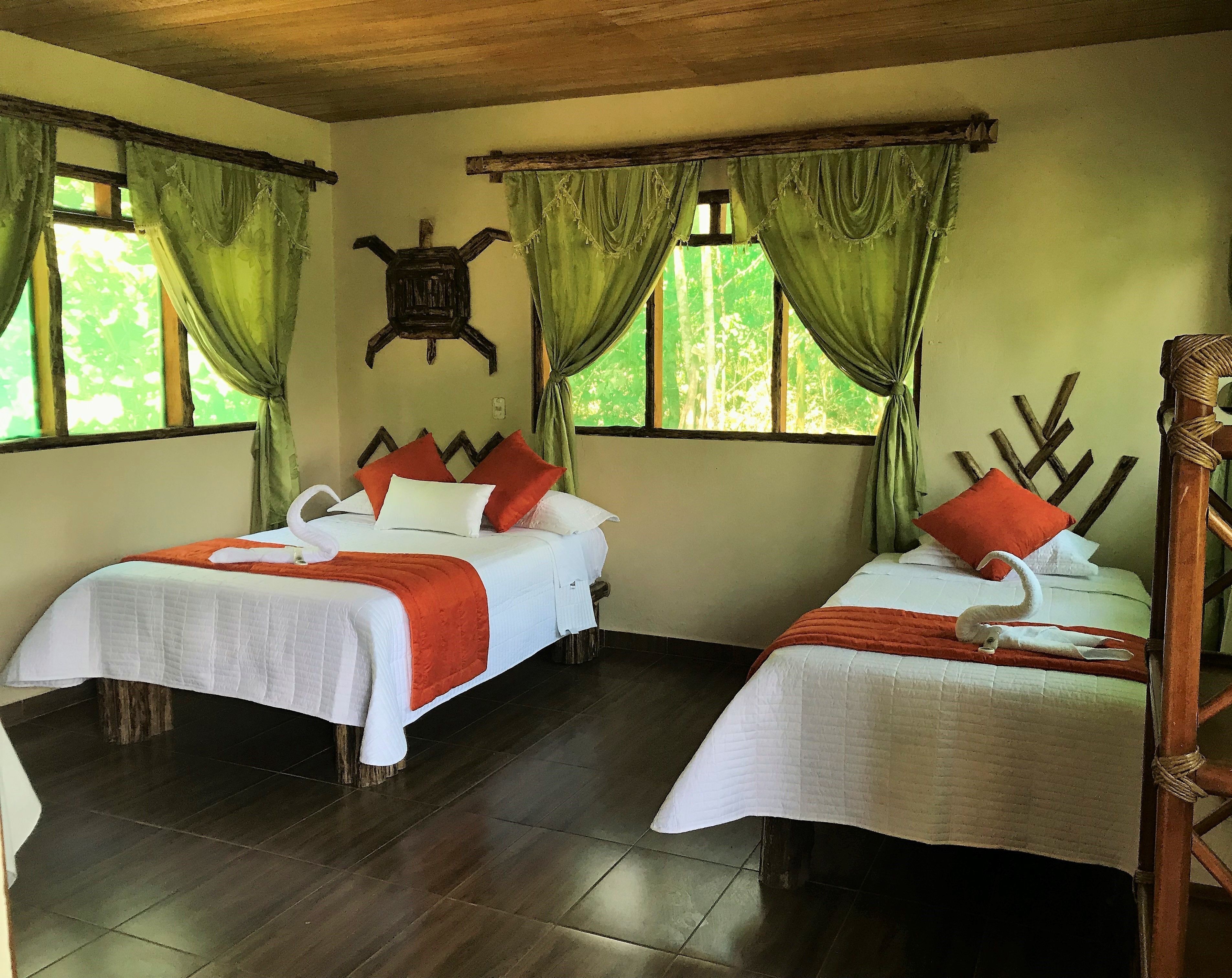 A room with two beds, each with white bedding and orange accents, wooden headboards, and green curtains.
