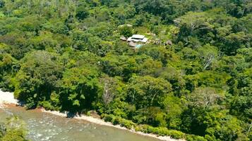 Une vue aérienne d’une propriété isolée, entourée d’une forêt dense, avec un petit bâtiment et une piscine.