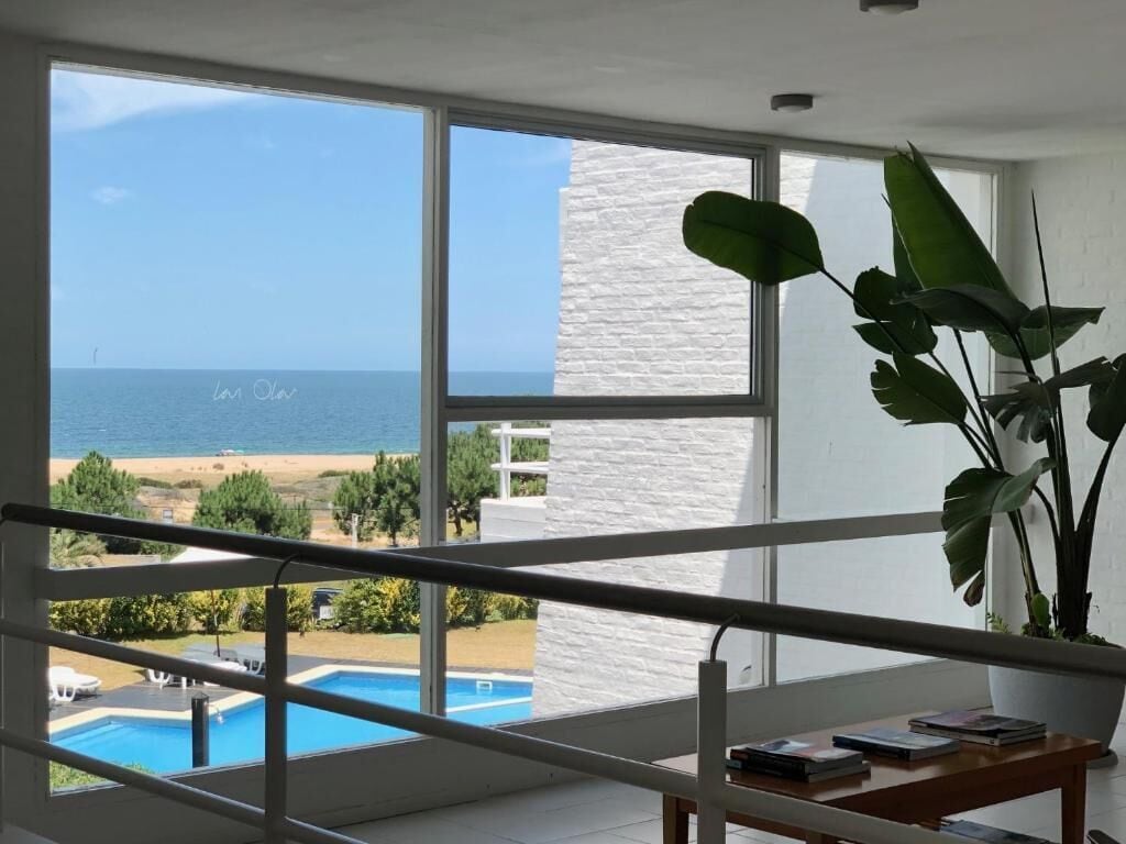 Habitación con un amplio ventanal que da a una playa y una piscina.