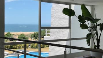 Habitación con un amplio ventanal que da a una playa y una piscina.