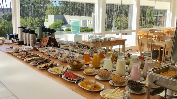 Un buffet proposant une variété de plats et de boissons, disposés sur une longue table, avec vue sur les arbres à l’extérieur.