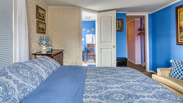 A bedroom with a large bed, a dresser, and a chair. There is a door leading to another room.