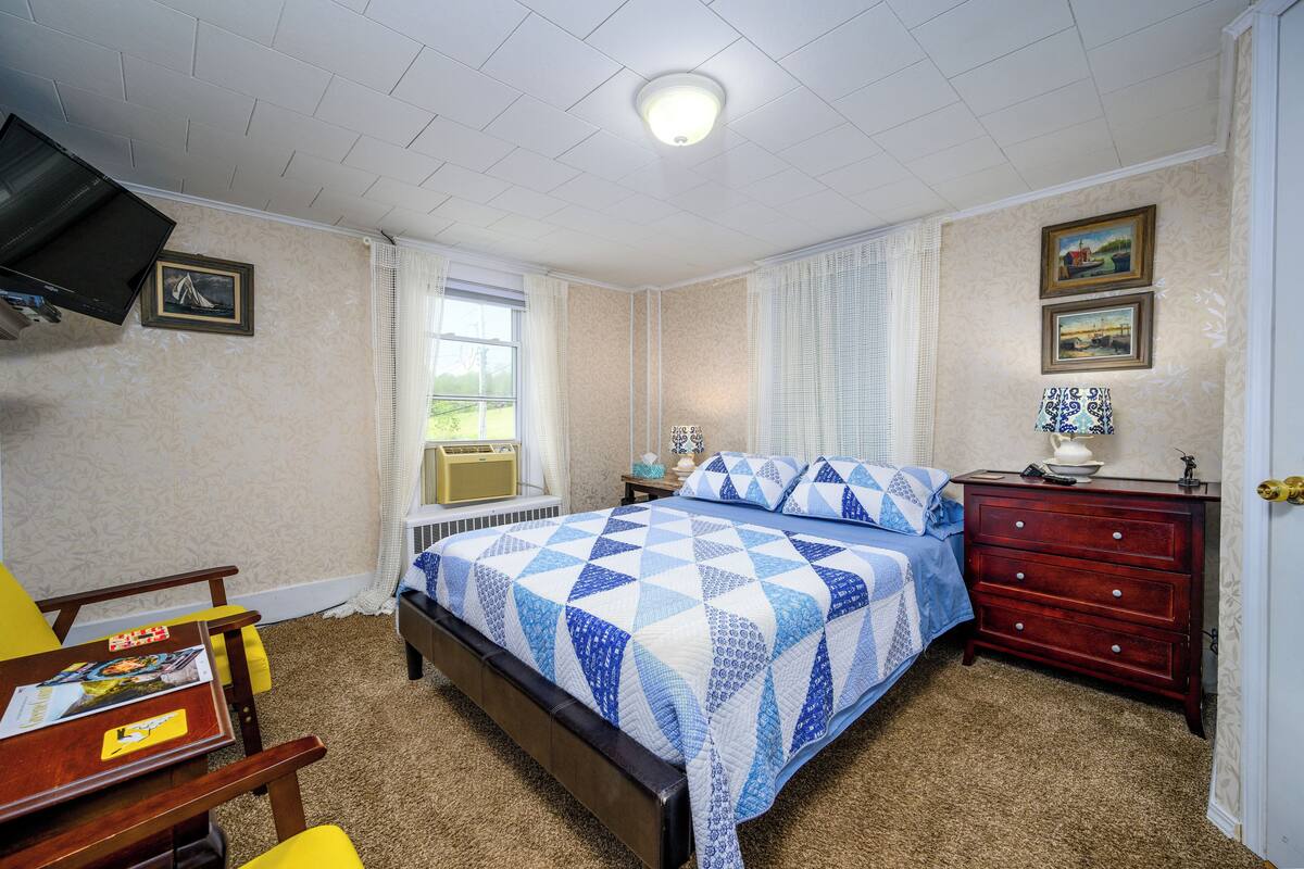 A bedroom with a bed, a dresser, a chair, a television, and a window.