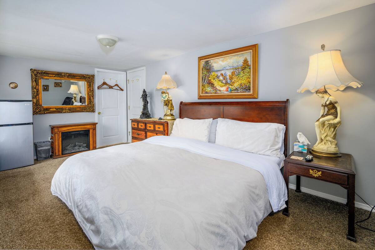 A hotel room with a large bed, a dresser, a mirror, a painting, and two lamps.