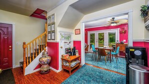 A well-lit hallway with a wooden staircase, a decorative vase, and a dining area with a table and chairs. - Mountain Treasure B&B (Maplecrest)