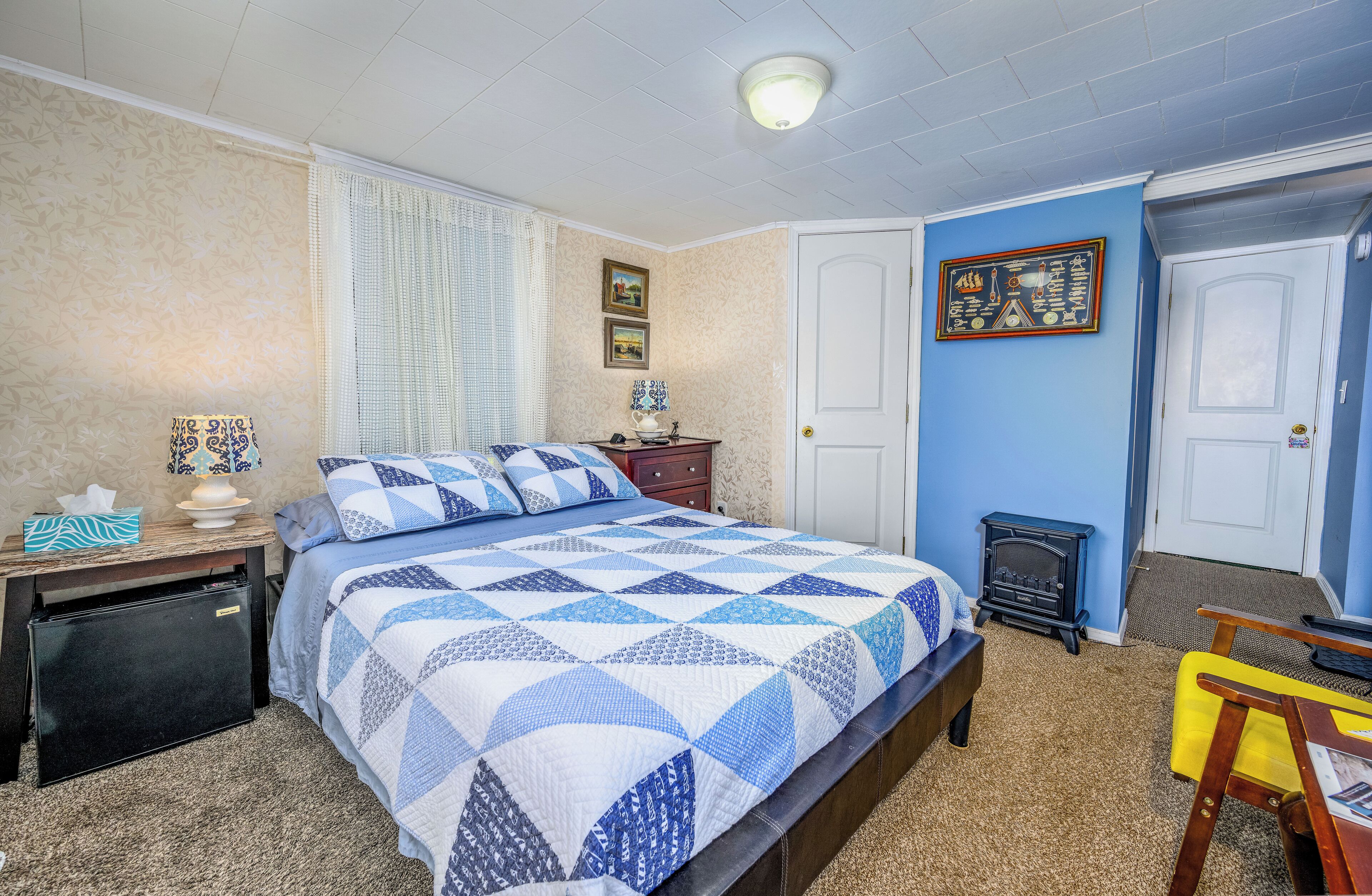 Een slaapkamer met een bed, nachtkastje, dressoir, bureau, stoel, verwarming en een deur.