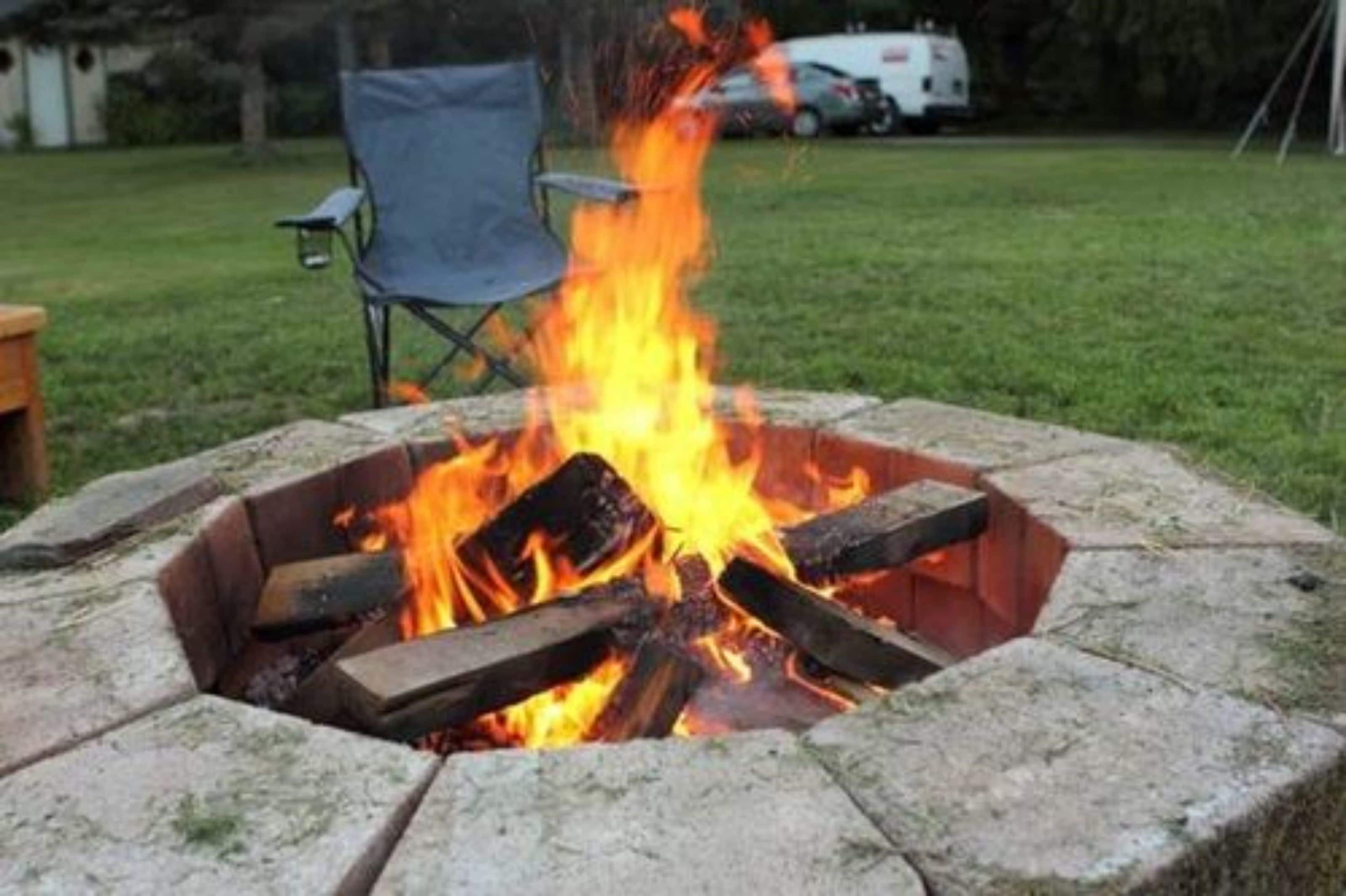 A fire pit with burning logs, surrounded by stone.
