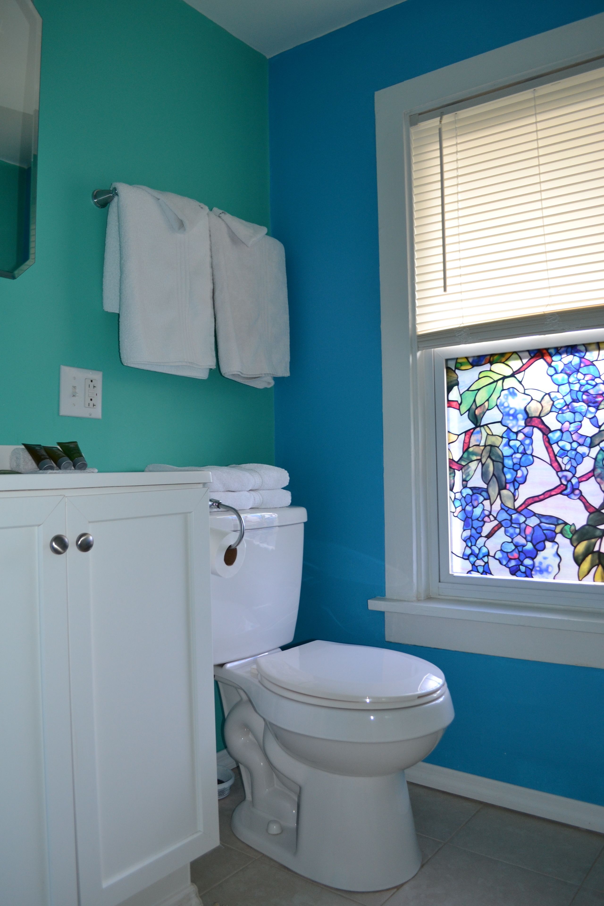 A bathroom with a white toilet, a white cabinet, and a window with a stained glass design.